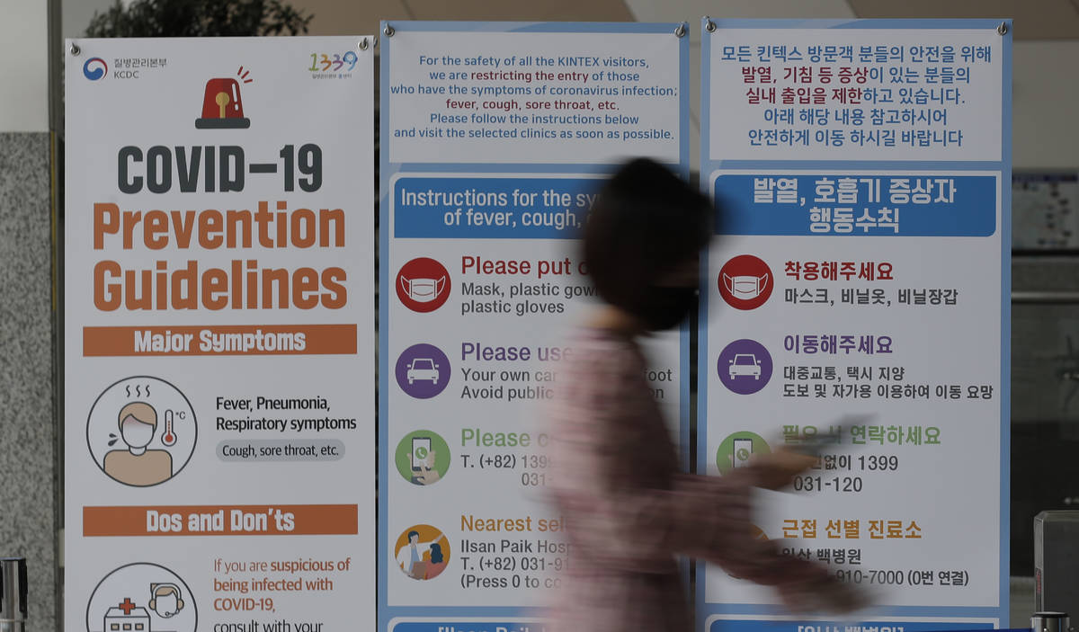 A woman wearing a face mask walks near a banner showing precautions against the new coronavirus ...