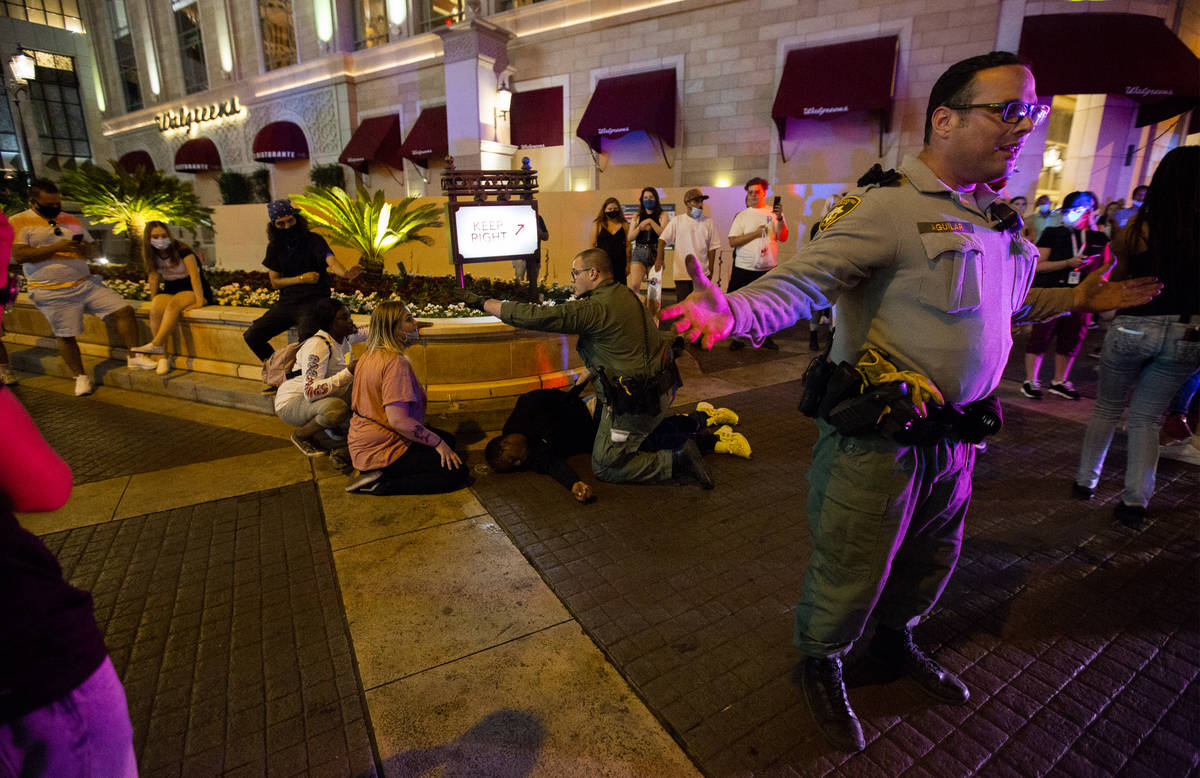 Las Vegas Metropolitan Police officers ask protesters to stand back as an officer kneels on a m ...
