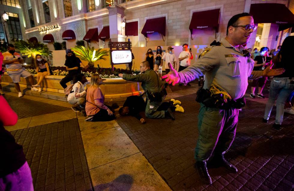 Las Vegas Metropolitan Police officers ask protesters to stand back as an officer kneels on a m ...