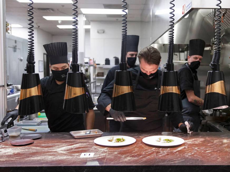 Chef Yuri Szarzewski, top/right, wears a protective mask while preparing food in the kitchen at ...