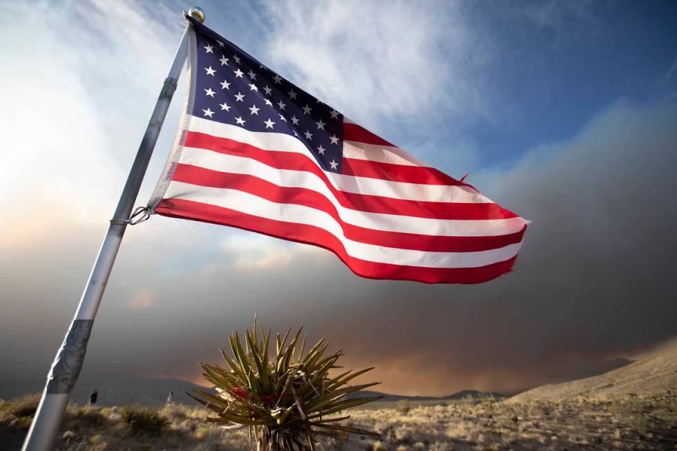 An American flag blows in the wind as the Mahogany Fire burns in the background at Mount Charle ...