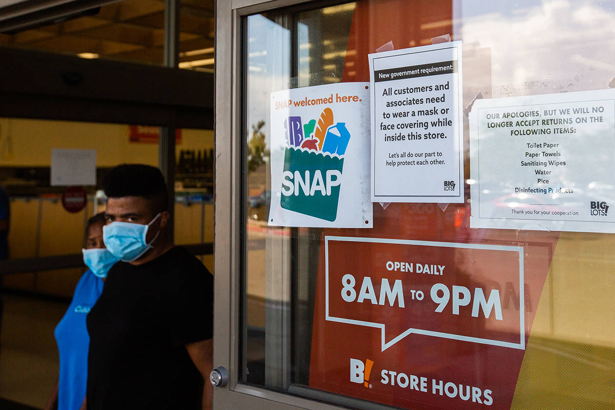 Customers wearing masks leave Big Lots next a sign stating that masks are required to enter in ...