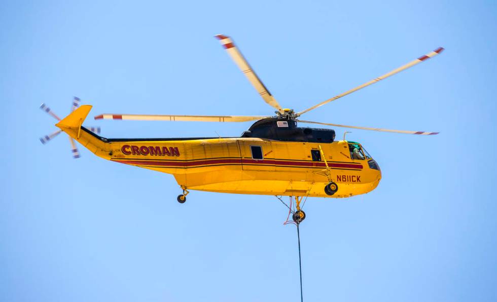 A helicopter with water bucket refills from a large water tank off Kyle Canyon Road for another ...