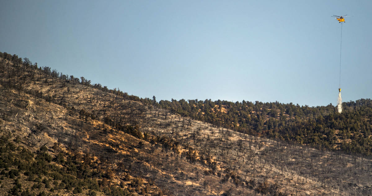 A helicopter with water bucket makes another drop over the Mahogany Fire on Mount Charleston on ...