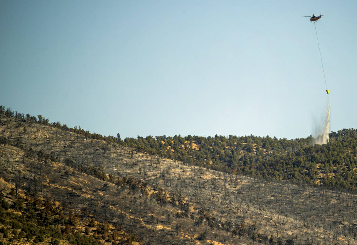 A helicopter with water bucket makes another drop over the Mahogany Fire on Mount Charleston on ...