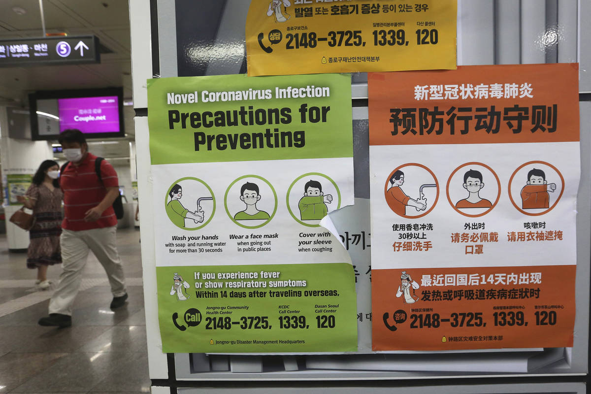 People wearing face masks pass by posters about precautions against new coronavirus at a subway ...