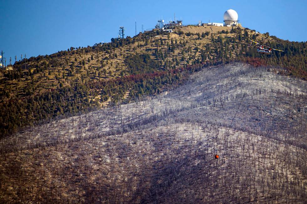 A helicopter with water bucket returns for another drop over the Mahogany Fire on Mount Charles ...