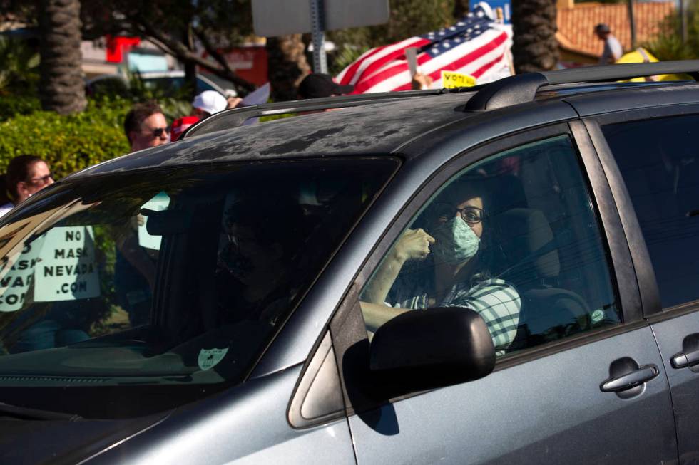 A passing motorist points to her mask as she passes the "No Mask Protest" at the inte ...