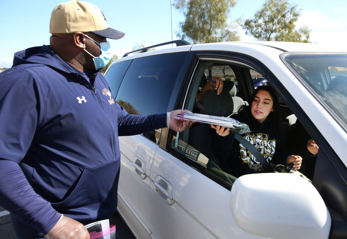 Marcus Teal, left, football and softball coach, hands out a Chromebook to Samantha Martin, seni ...