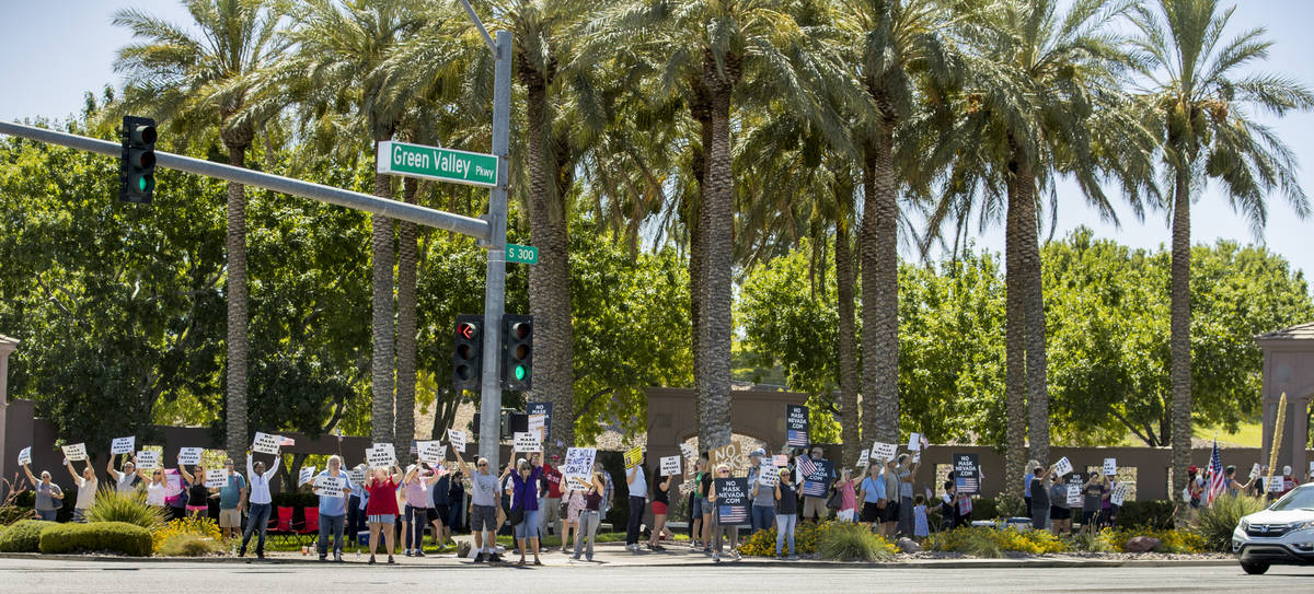 Protesters hold signs and wave to cars during a No Mask Nevada PAC rally along South Green Vall ...