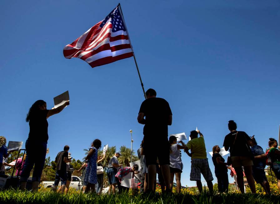 A protester holds an American flag as others wave signs and chant slogans during a No Mask Neva ...