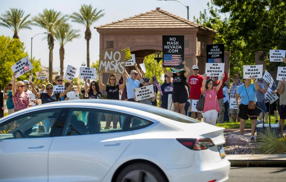 Protesters hold signs and wave to cars during a No Mask Nevada PAC rally along South Green Vall ...