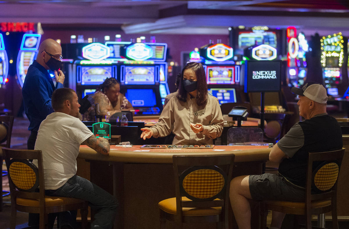 A dealer wearing a protective face mask talks with gamblers playing blackjack at Treasure Islan ...