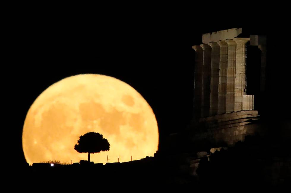 The moon rises behind the columns of the ancient marble Temple of Poseidon at Cape Sounion, abo ...