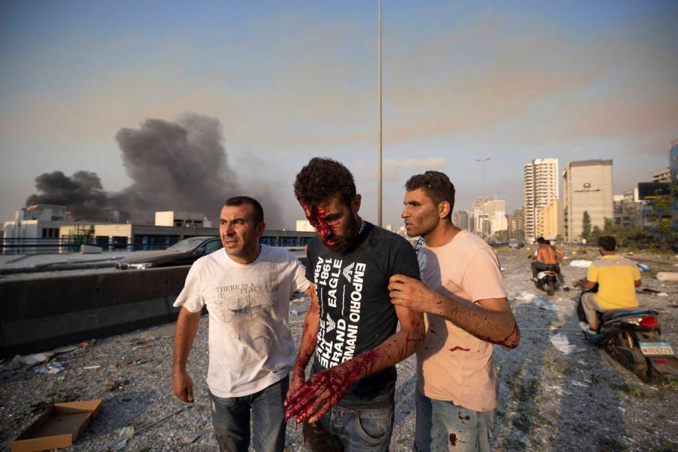 People help a man wounded in a massive explosion in Beirut, Lebanon, Tuesday, Aug. 4, 2020. Mas ...