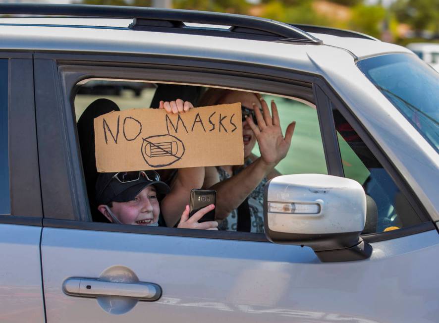 A passenger with sign and driver show their support as they pass by a No Mask Nevada rally to o ...