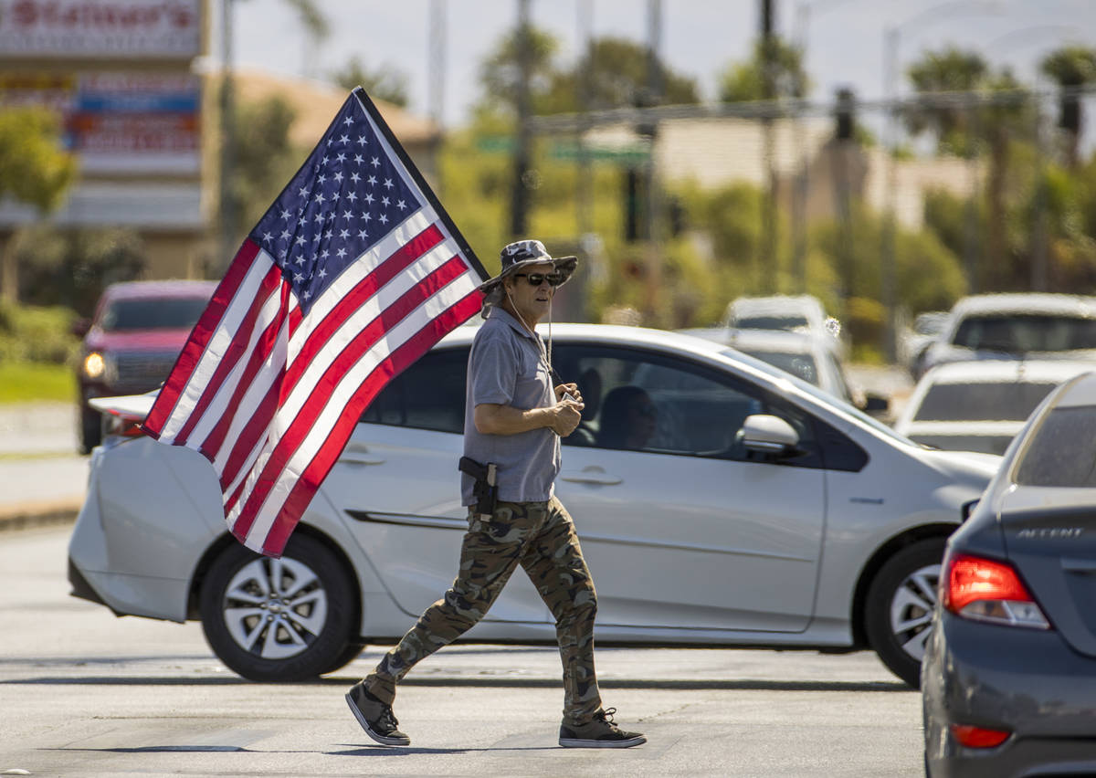 A supporter carrying a flag makes another cross of traffic during the No Mask Nevada rally to o ...