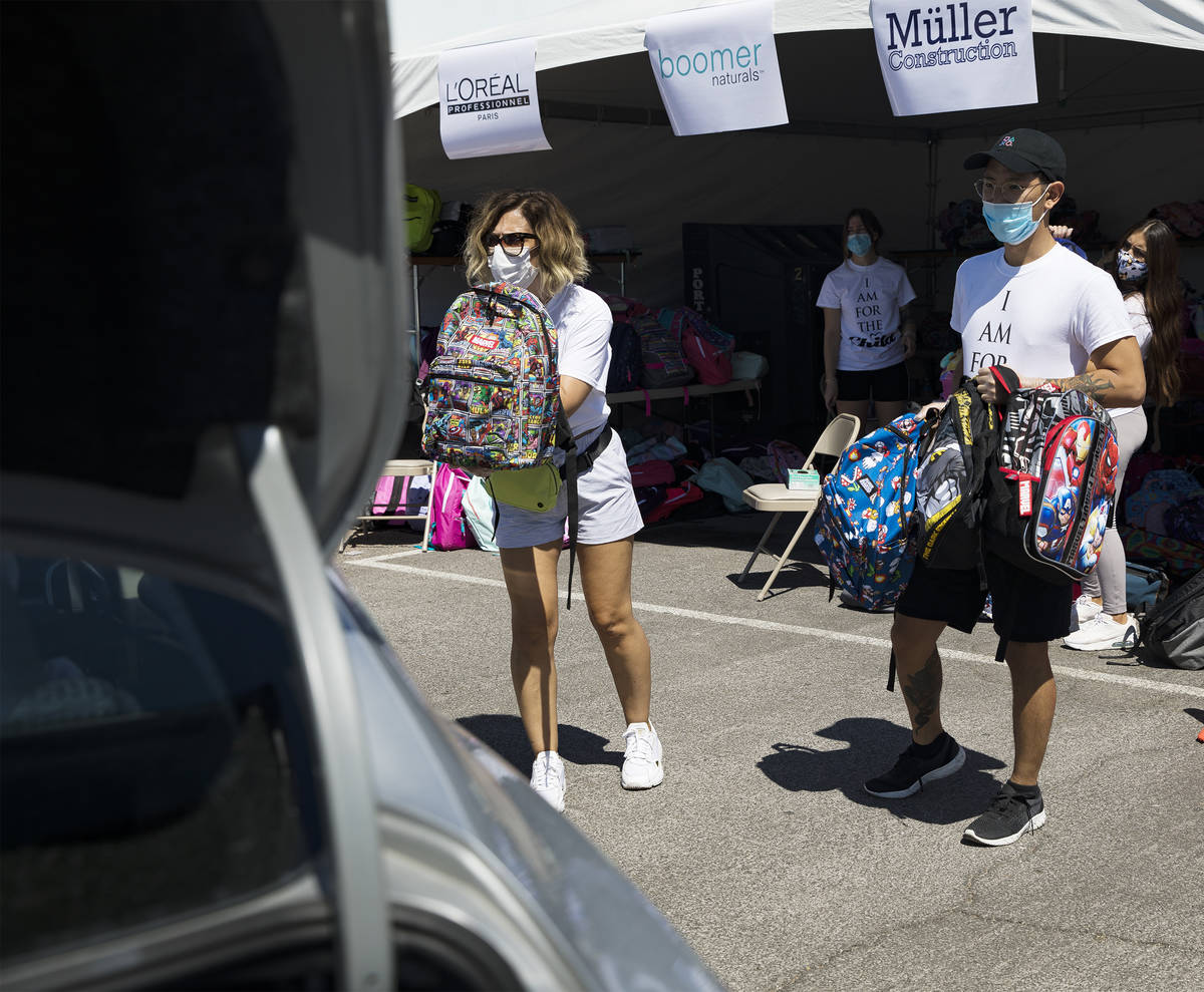 Volunteers Theresa Broussard, left, and Dillon Mones, right, show backpacks to foster kids in a ...