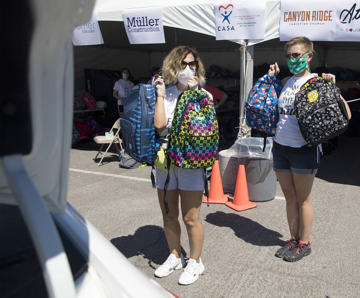 Volunteers Theresa Broussard, left, and Alexis Von Schlieder, right, show backpacks to foster k ...