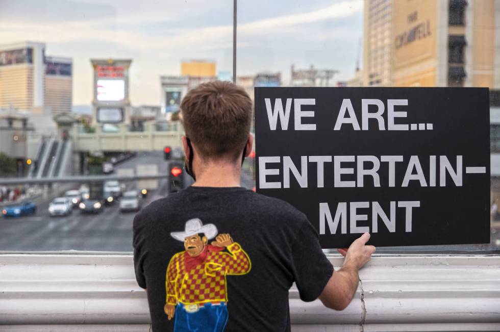 Tylor Godshall holds a sign on a pedestrian bridge while watching a motorcade of his peers pass ...