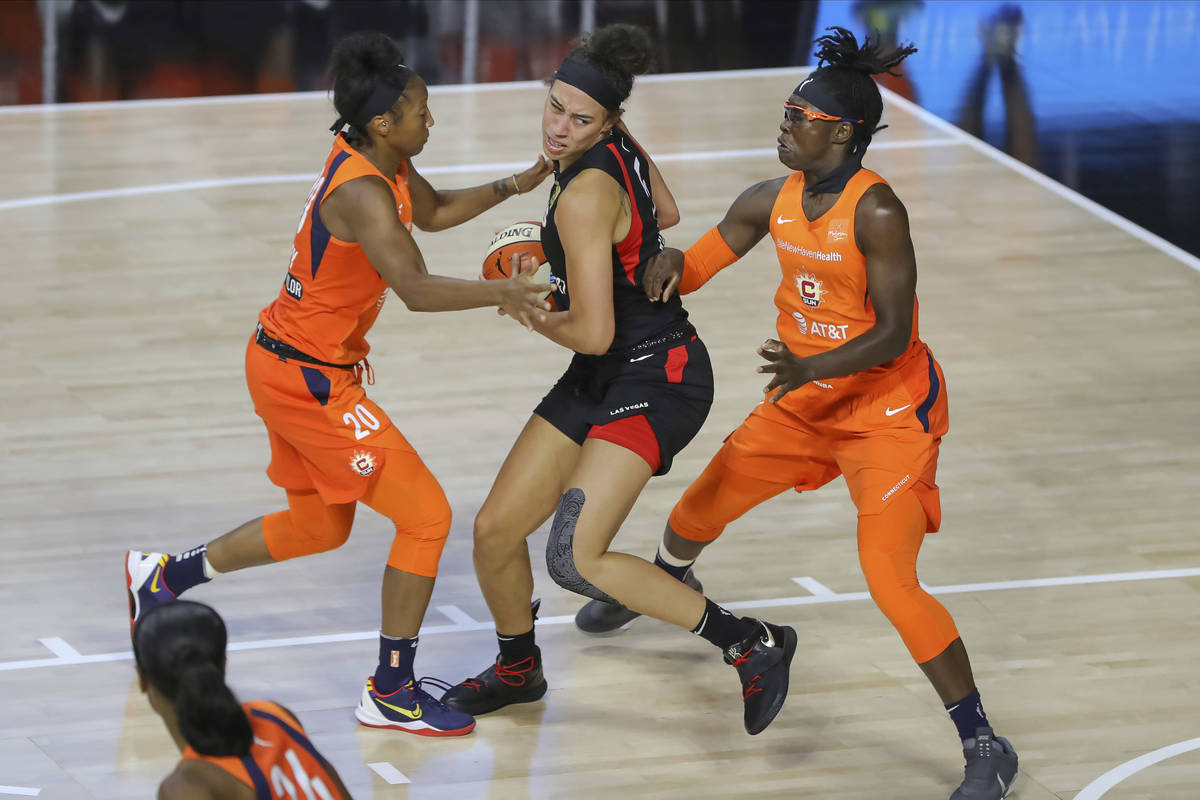 Las Vegas Aces' Dearica Hamby drives between Connecticut Sun's Briann January (20) and Essence ...