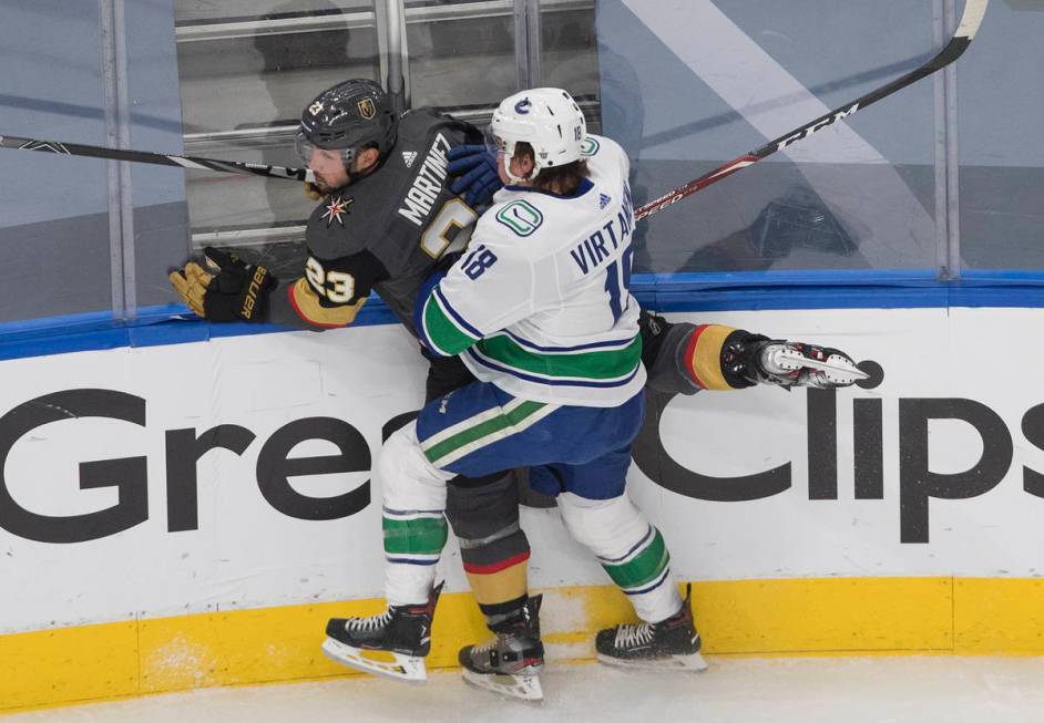 Vegas Golden Knights' Alec Martinez (23) is checked by Vancouver Canucks' Jake Virtanen (18) du ...