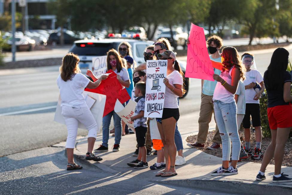 People hold up signs while participating in a demonstration in support of reopening public scho ...