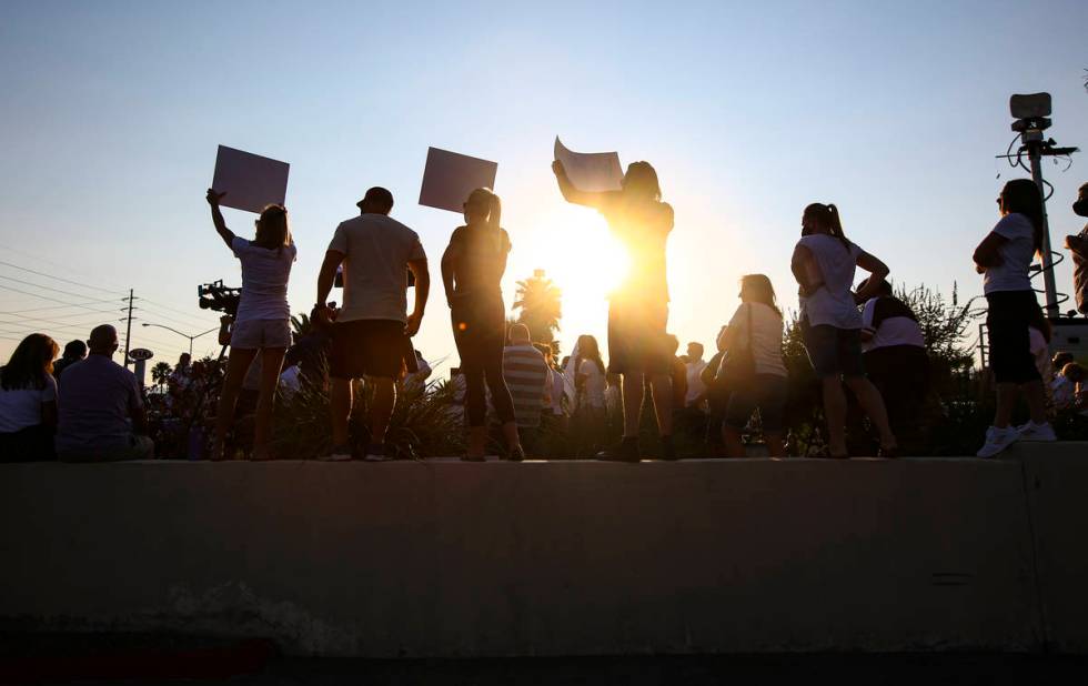 People hold up signs while participating in a demonstration in support of reopening public scho ...