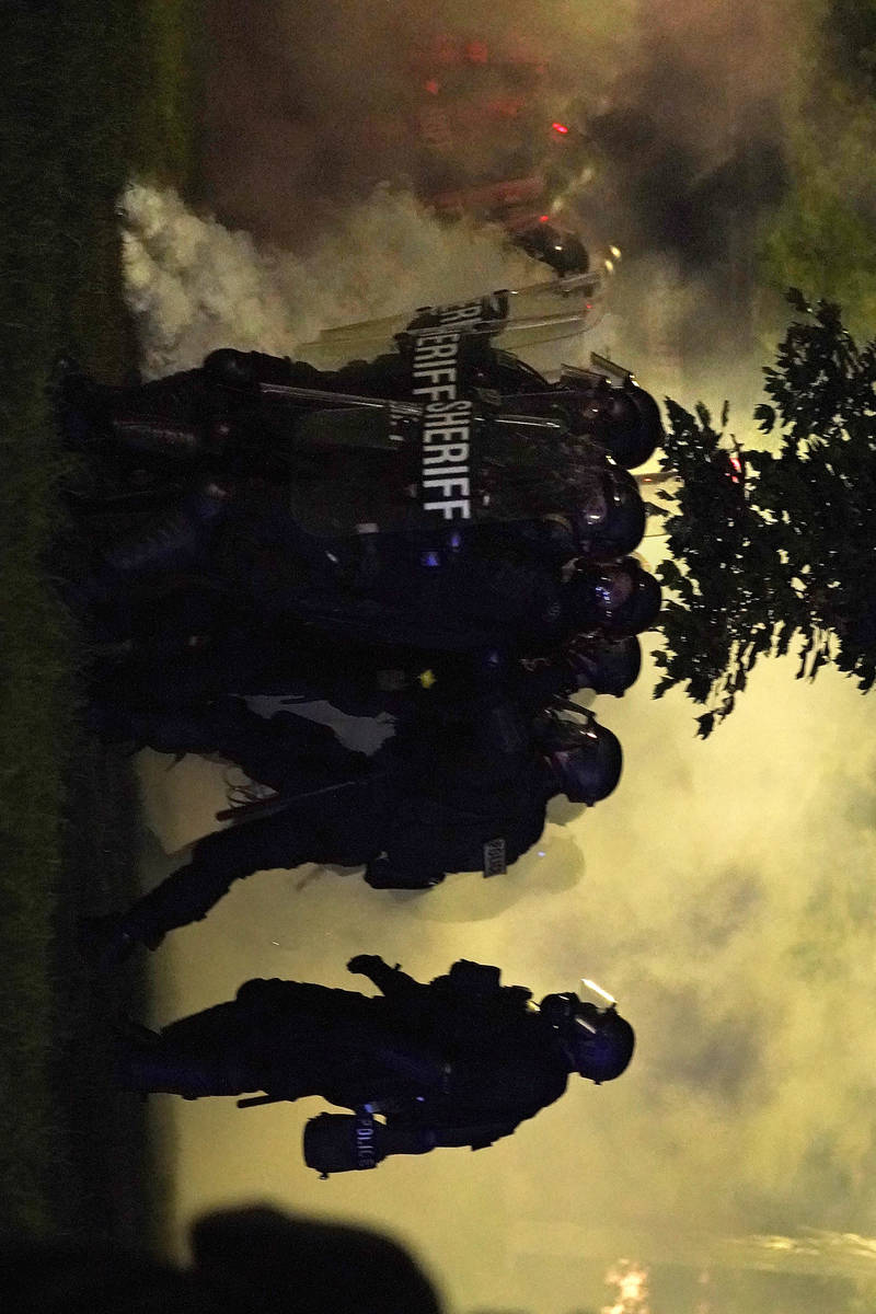 Police in riot gear clear a park during clashes with protesters outside the Kenosha County Cour ...