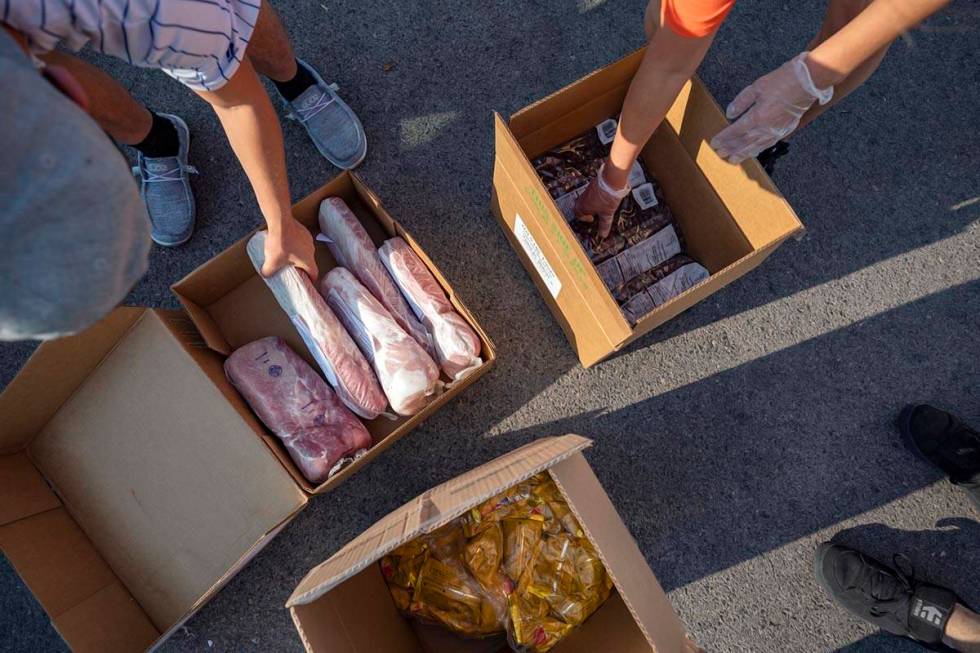 Three Square Food Bank volunteers grab frozen pork tenderloin, frozen blueberries and sack pack ...