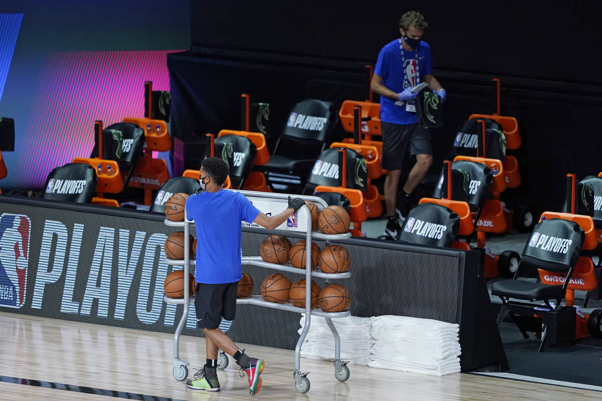 Workers clear items from the Milwaukee Bucks bench after the scheduled start time of an NBA bas ...