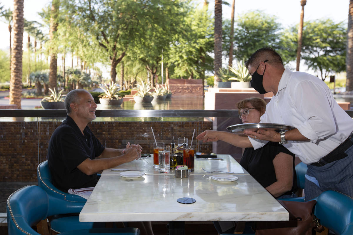 Server Erik Villaneuva serves Michael Diliberto and Colleen Diliberto drinks on the patio at Os ...