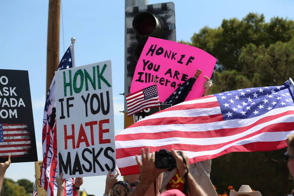 People participating in a No Mask Nevada PAC rally block the sign of a counter protester at Sun ...