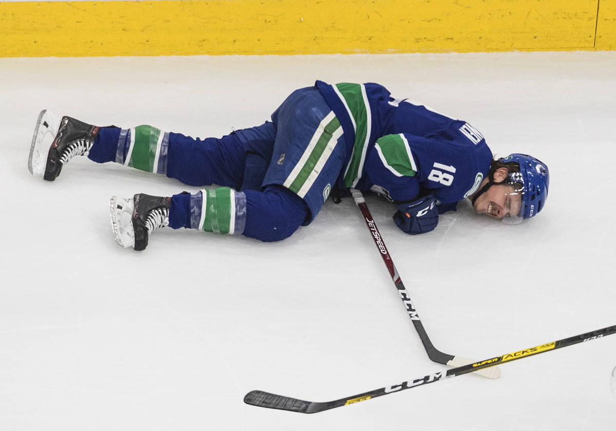 Vancouver Canucks' Jake Virtanen (18) lies on the ice after taking a hit along the boards from ...