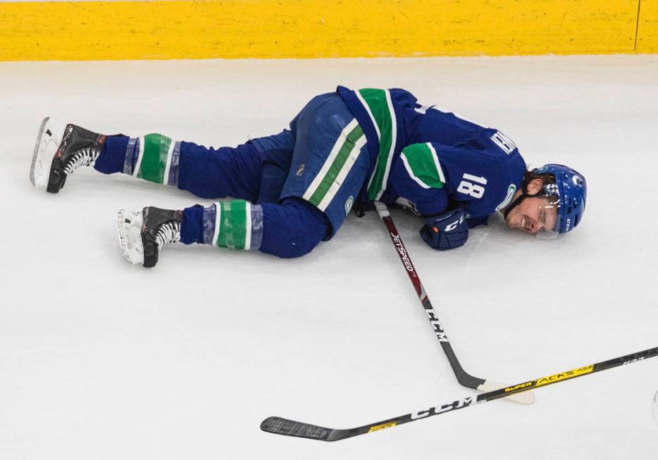 Vancouver Canucks' Jake Virtanen (18) lies on the ice after taking a hit along the boards from ...