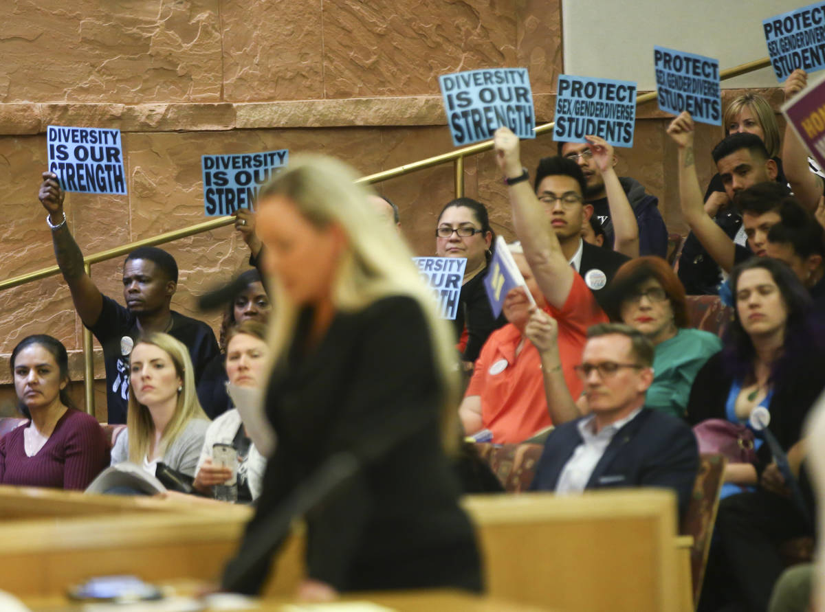Aimee Hairr speaks as members of the audience hold up signs in support during public comment ab ...