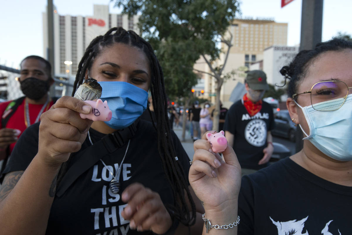 Monique Malett, left, and Asia Thornton, right, hold up toy pigs, which they squeak when police ...