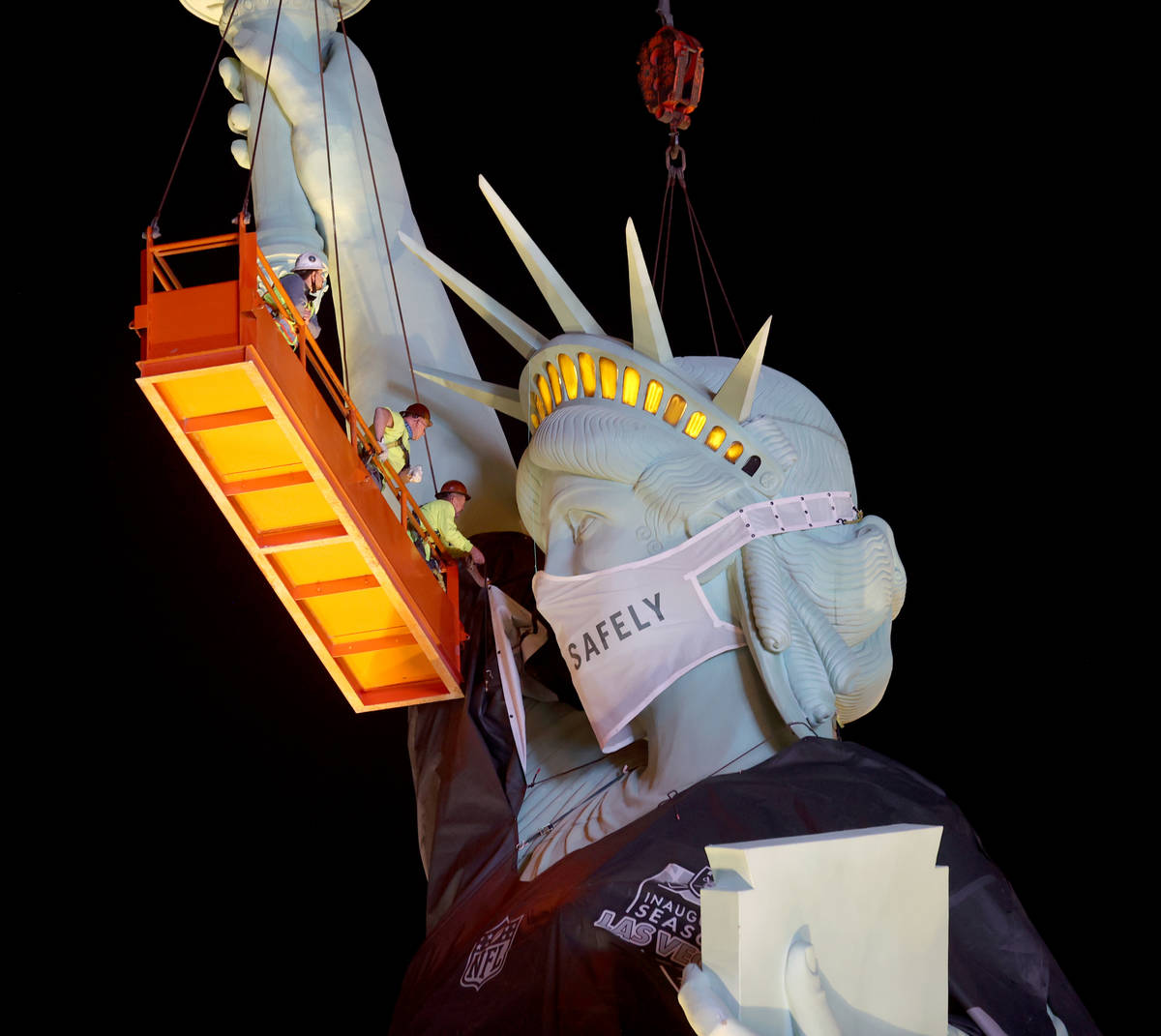 Workers install a a Las Vegas Raiders jersey on the Statue of Liberty replica at New York-New Y ...