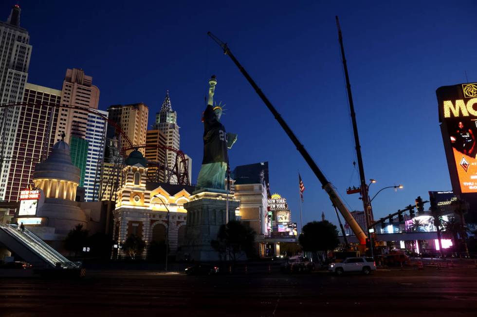 Workers install a a Las Vegas Raiders jersey on the Statue of Liberty replica at New York-New Y ...