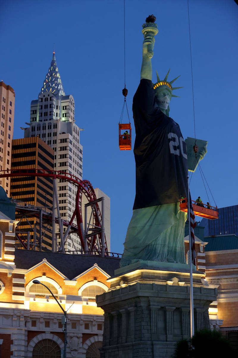 Workers install a a Las Vegas Raiders jersey on the Statue of Liberty replica at New York-New Y ...