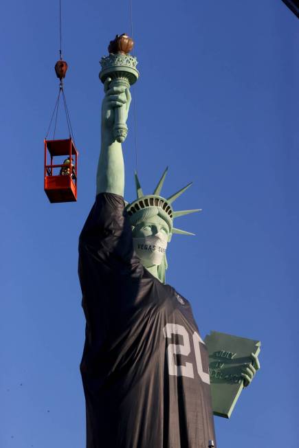 Workers install a a Las Vegas Raiders jersey on the Statue of Liberty replica at New York-New Y ...