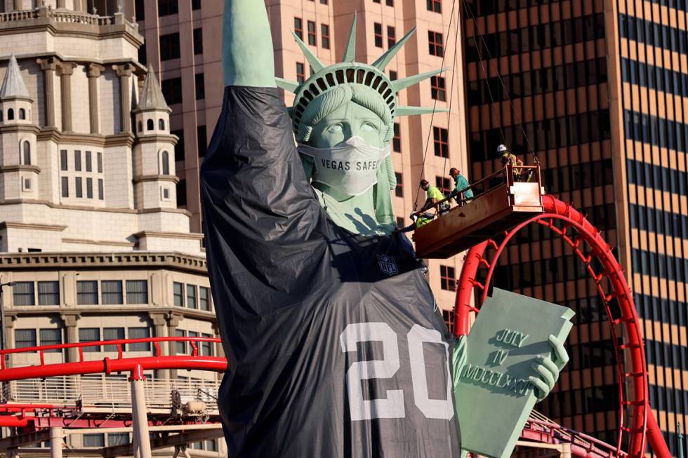 Workers install a a Las Vegas Raiders jersey on the Statue of Liberty replica at New York-New Y ...