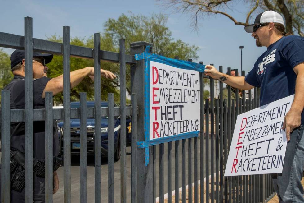 A security guard instructs Jon Berry, right, to take down a sign he attached to a fence in fron ...