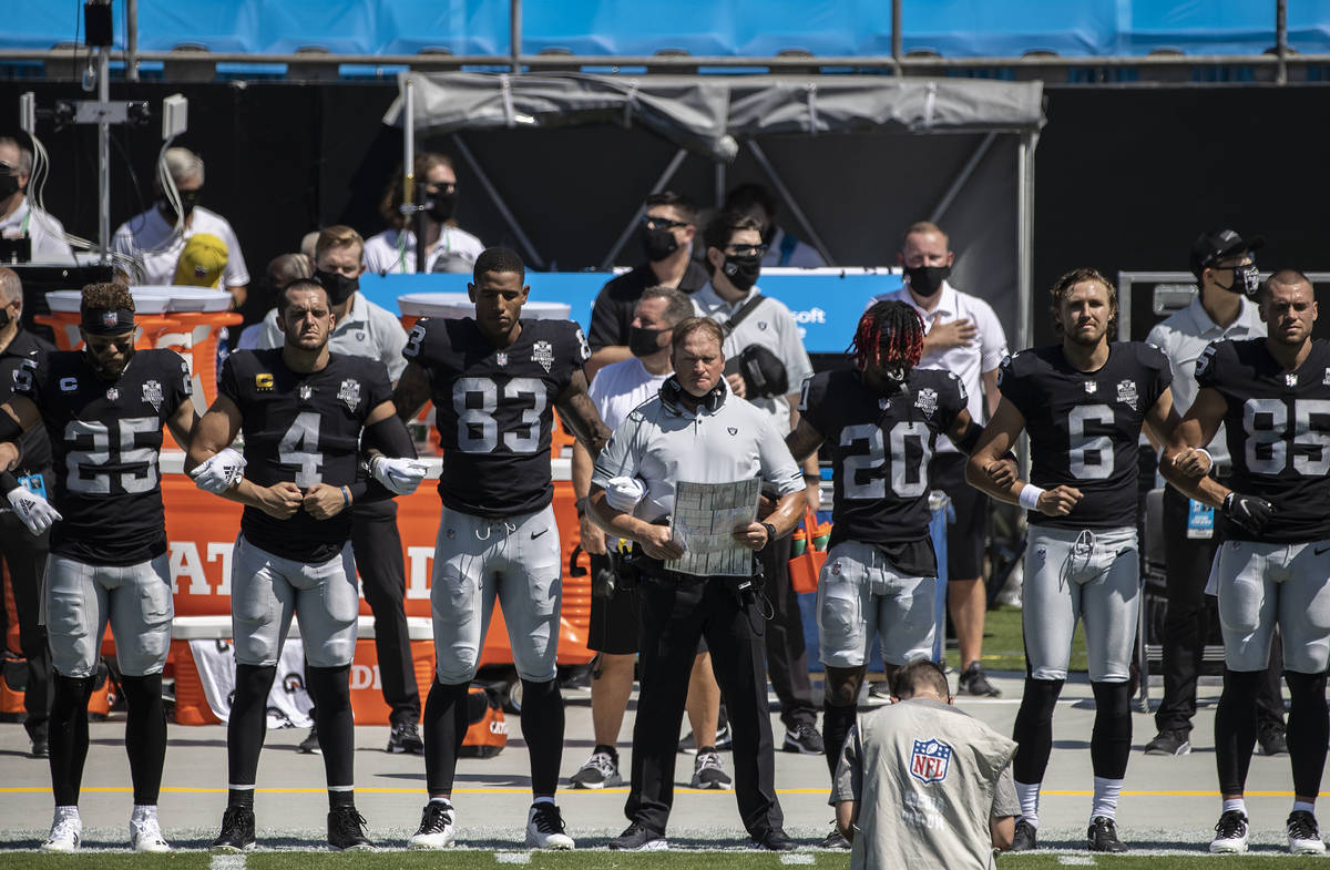 Las Vegas Raiders head coach John Gruden, middle, locks arms with his players during the nation ...