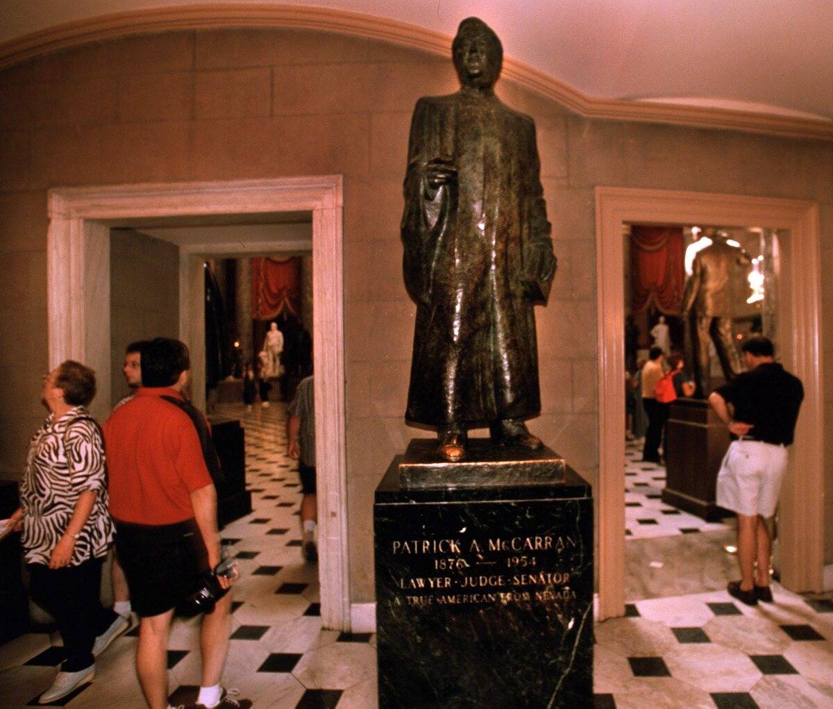 Tourist pass the statue of Nevada Senator Pat McCarran, located in the National Statuary Hall i ...