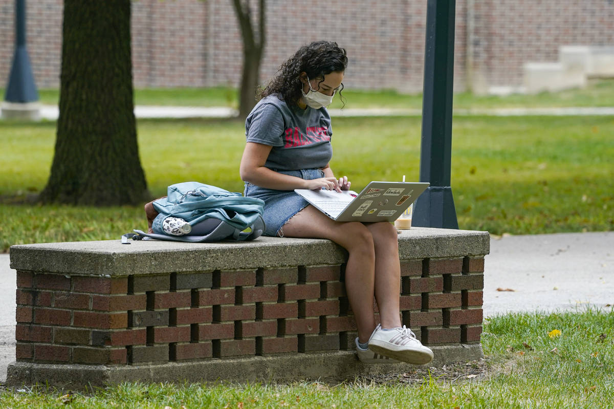 A masked student works on her laptop on the campus of Ball State University in Muncie, Ind., Th ...