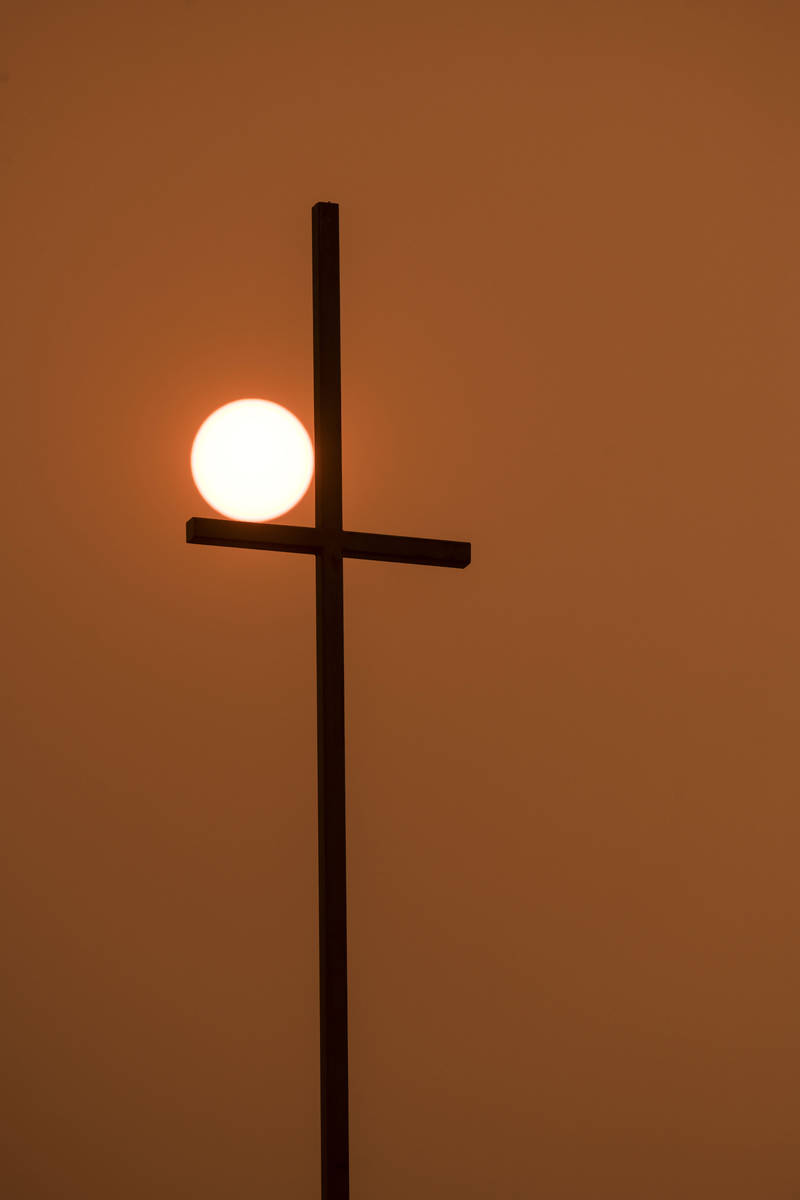 In a sky with wildfire smoke, the rising sun shines orange behind a church's cross in Walla Wal ...