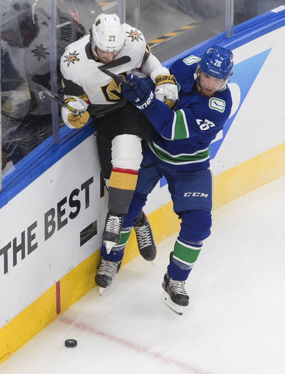 Vegas Golden Knights' Shea Theodore (27) is checked by Vancouver Canucks' Antoine Roussel (26) ...