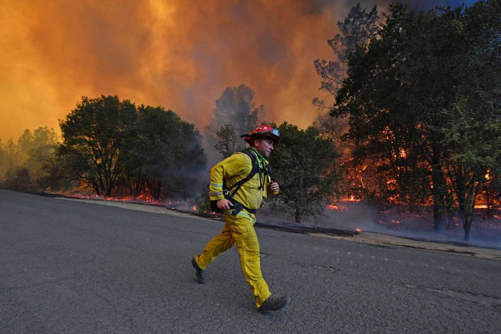 A firefighter runs to his firetruck while protecting a home along Crystal Springs Road while ba ...