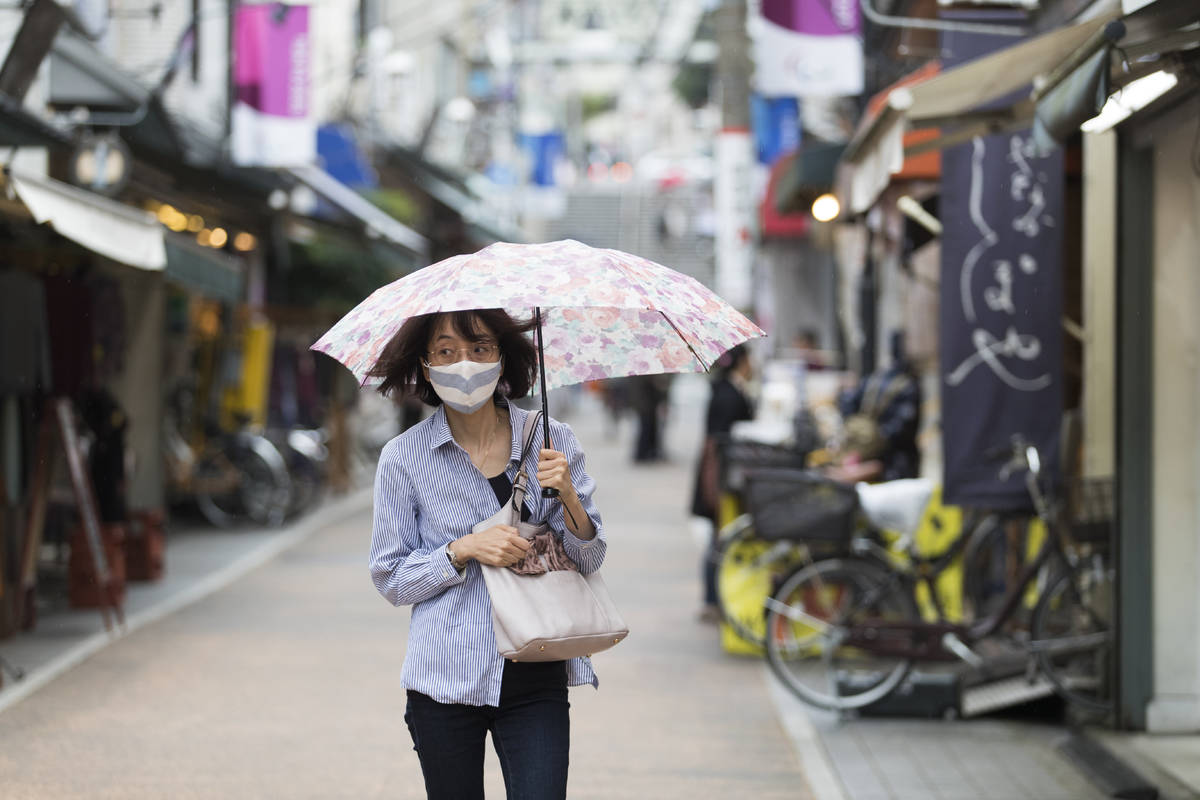 A woman with a face mask walks through a shopping street in the rain in Tokyo on Thursday, Oct. ...